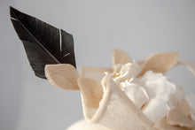 Carica l'immagine nel visualizzatore di Gallery, Toque composta da un ricciolo di sisal che racchiude un tralcio di gardenie in lino da cui spicca una piuma nera. Poggia e scorre su un cerchietto in tinta. Un must della collezione Chapeau Flambe White Bridal.