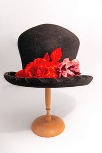 Cappello artigianale made in Italy in morbido feltro velour di lapin neroguarnito da una coppia di rose rosse di velluto e dall'ala bordata torçon da un prezioso nastro di velluto nero. Top hat tra i più iconici e amati da sempre