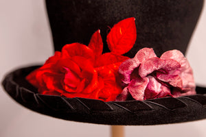 Cappello artigianale made in Italy in morbido feltro velour di lapin neroguarnito da una coppia di rose rosse di velluto e dall'ala bordata torçon da un prezioso nastro di velluto nero. Top hat tra i più iconici e amati da sempre